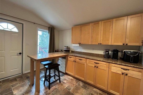 Kitchen with light wood cabinets, granite countertops, island, and a door to outside. - 217 5th Street Nw, Minnedosa