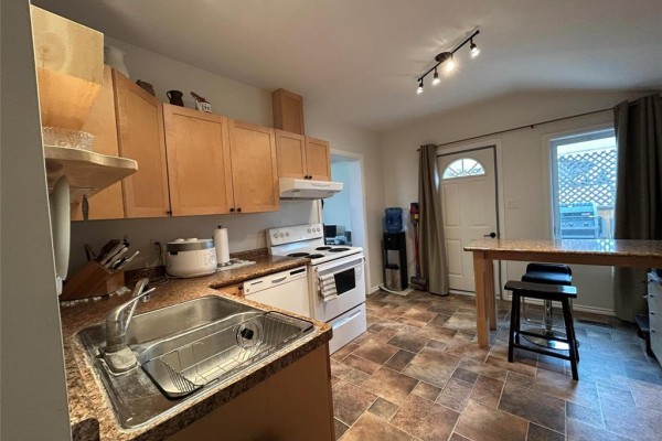 Kitchen with a sink, dishwasher, white stove, wood cabinets, and a breakfast bar. - 217 5th Street Nw, Minnedosa