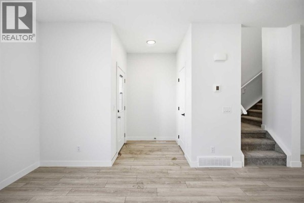Empty entryway with light wood laminate flooring, white walls, and a staircase leading upstairs. - 217 Bridgeport Gate, Chestermere