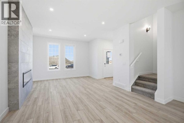 Living room with light wood laminate flooring, white walls, a gas fireplace, and stairs to the right. - 217 Bridgeport Gate, Chestermere