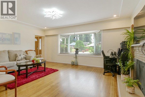 Living room with a large bay window, beige sectional sofa, red rug, and hardwood floors. - 21727 Ridgeway Crescent, Maple Ridge