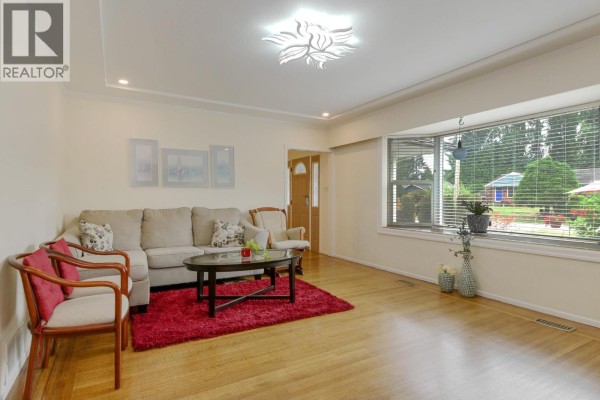 Living room facing a bay window with a sofa and chairs, hardwood floors, and a red rug. - 21727 Ridgeway Crescent, Maple Ridge