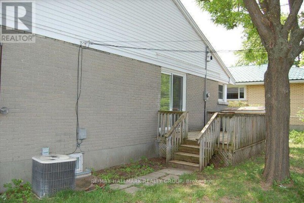 Rear exterior view of a house with a wooden deck, mature tree, and an air conditioning unit on the side. - 2173 Rushton Road, Ottawa