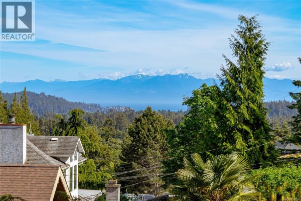 View from a balcony over trees towards distant mountains and a body of water. - 2175 Firwood Pl, Sooke