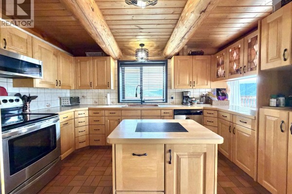 Bright kitchen with light wood cabinets, a central island, and a window overlooking a scenic view. - 2175 White Road, Williams Lake