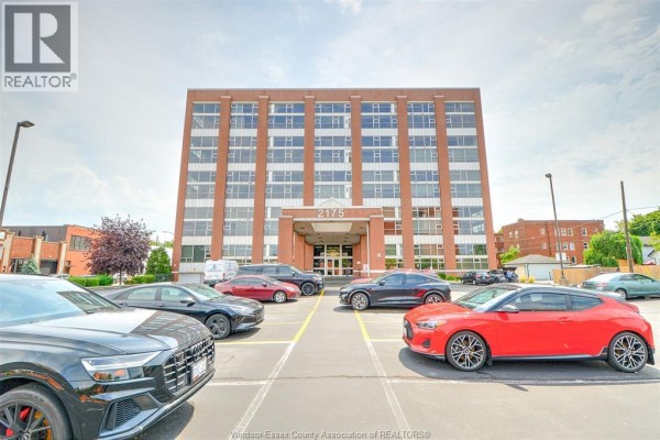 Parked cars in front of a tall red brick apartment building. - 2175 Wyandotte Street East Unit# 105, Windsor