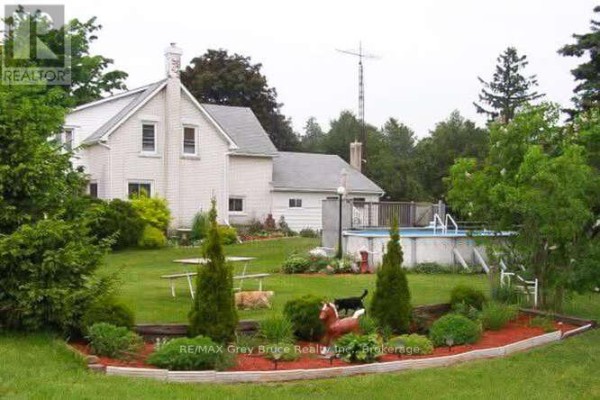 Rear view of the white house with a green lawn and fenced pool. - 217590 Concession 3 Concession, Georgian Bluffs