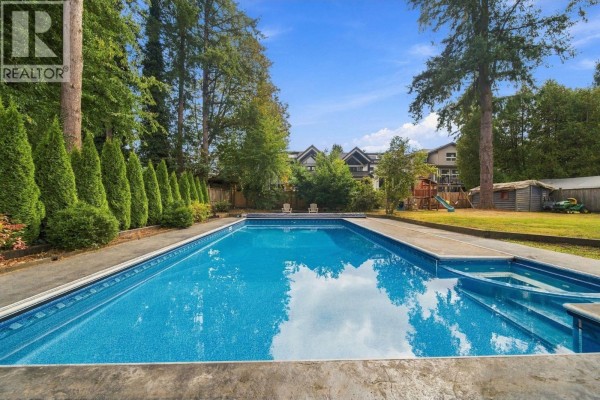 Rectangular blue swimming pool with steps and lounge chairs in a backyard with a lawn. - 21768 117 Avenue, Maple Ridge