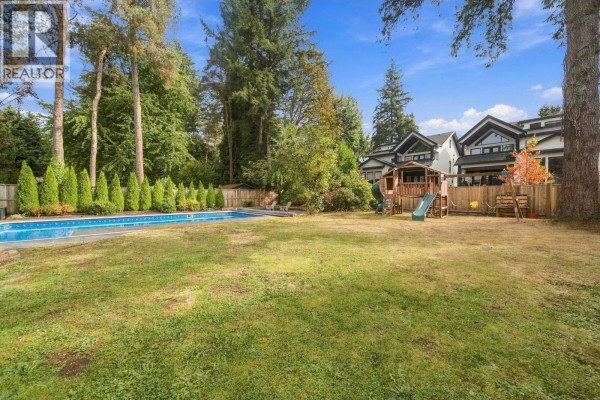 Backyard view showing a swimming pool, children's playset, and fenced perimeter with trees. - 21768 117 Avenue, Maple Ridge
