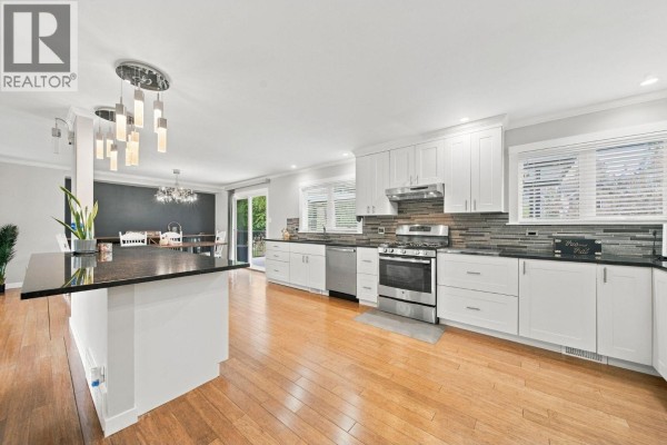 Modern white kitchen with stainless steel appliances, granite countertops, and a large island. - 21768 117 Avenue, Maple Ridge