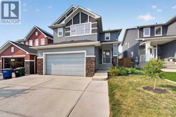 Front exterior view of a two-story house with a grey siding and stone accents. - 2177 Ravensdun Crescent Se, Airdrie