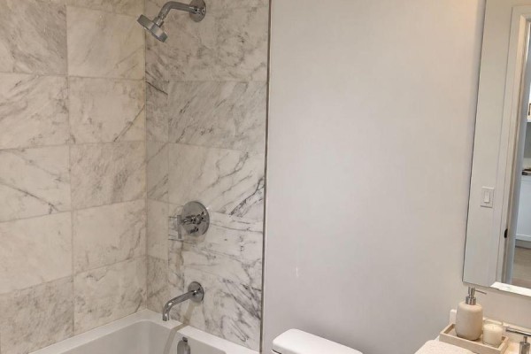 Bathroom with a bathtub, showerhead, white tile, and toilet, with a vanity mirror visible. - 218 - 2788 Bathurst Street, Toronto
