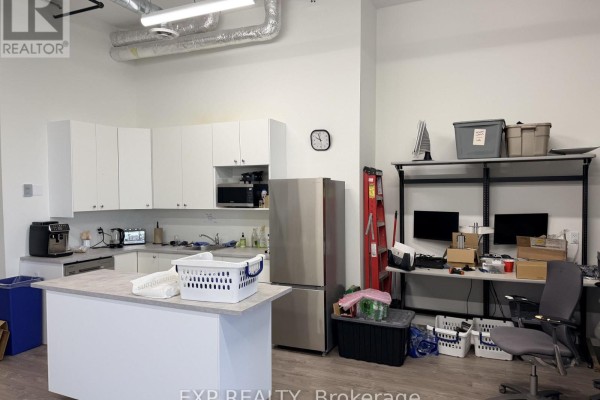 Office kitchen with white cabinets and island, stainless steel refrigerator and additional workstations. - 218 - 65 Denzil Doyle Court, Ottawa