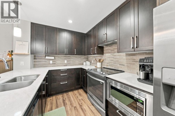 U-shaped kitchen with dark wood cabinets, quartz countertops, and stainless steel appliances. - 218 2495 Wilson Avenue, Port Coquitlam