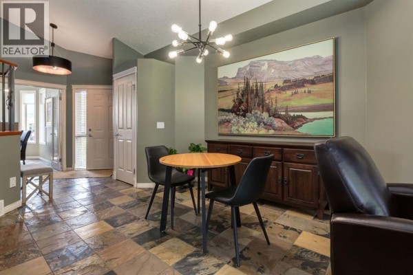 Dining area with a round table, two chairs, dark wood buffet, and large landscape art. - 218 Springbank Villas Sw, Calgary
