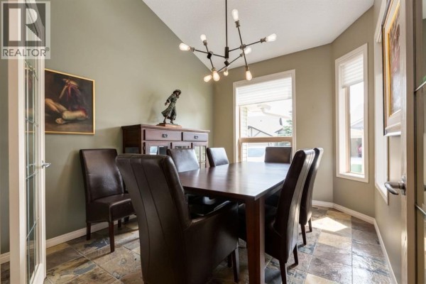 Formal dining room with a rectangular table, six leather chairs, and a modern chandelier. - 218 Springbank Villas Sw, Calgary