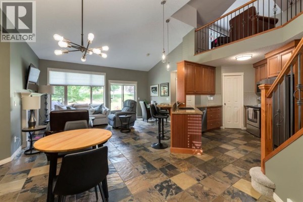 Open concept living area with a kitchen, dining space, and living room with a loft above. - 218 Springbank Villas Sw, Calgary