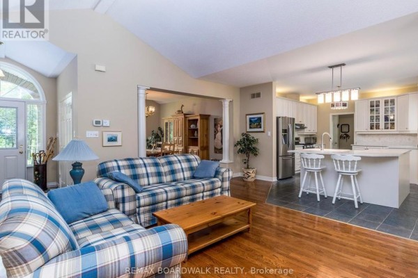 Living room with vaulted ceiling, hardwood floors, plaid sofas, and an open view to the white kitchen. - 2180 Conley Road, Ottawa
