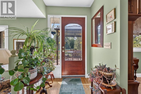 Interior entryway with light green walls, a wooden door, mirror, and abundant houseplants. - 2183 Daley Road, Tyendinaga