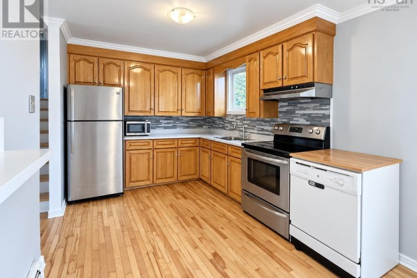 Kitchen with light wood cabinets, stainless steel appliances, and a backsplash with gray and white tiles. - 2183 Old Sambro Road, Williamswood