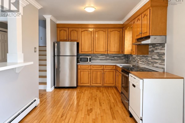 View of the kitchen with wood cabinets, stainless steel refrigerator, oven, and dishwasher, and stairs to the left. - 2183 Old Sambro Road, Williamswood