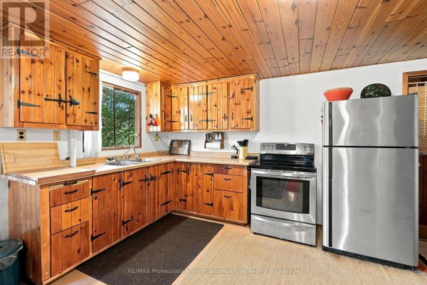 L-shaped kitchen with knotty pine cabinets, butcher block counters, stainless steel appliances, and a wood plank ceiling. - 2183 Trapper's Trail, Dysart Et Al