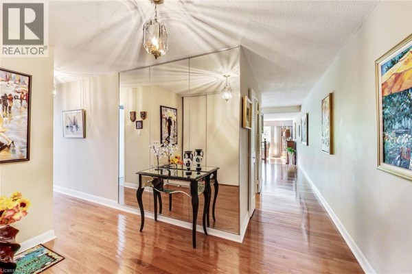 Apartment hallway with hardwood floors, mirrored wall, console table, and artwork. - 2185 Marine Drive Unit# 202, Oakville