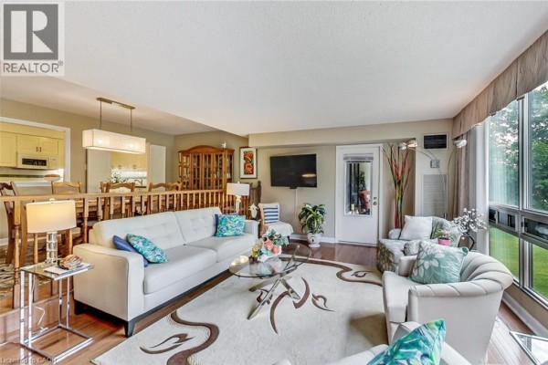 Living room with white sofas, a glass coffee table, dining area, and large window. - 2185 Marine Drive Unit# 202, Oakville