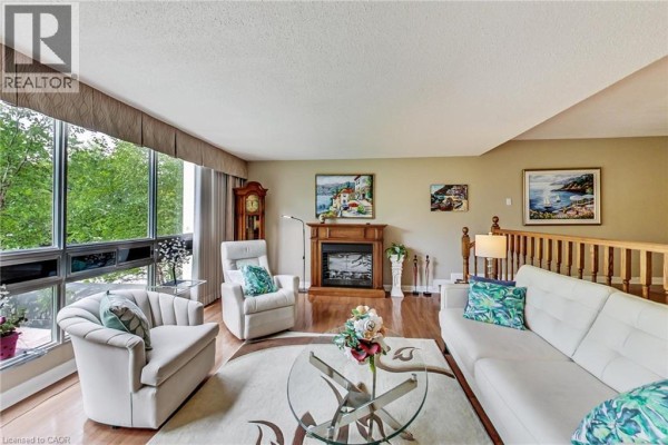 Living room with fireplace, armchairs, sofa, large windows with green tree views. - 2185 Marine Drive Unit# 202, Oakville