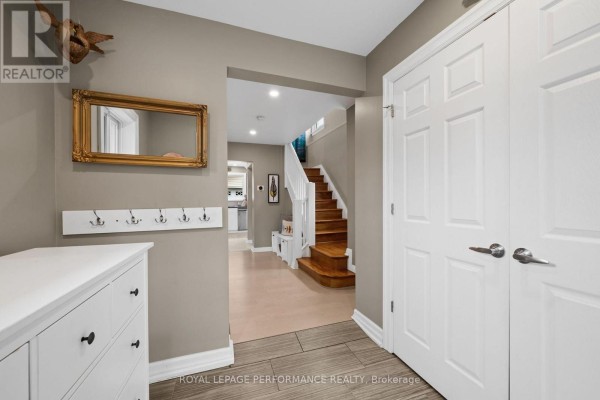 Foyer with a white chest, gold framed mirror, coat hooks, and view of the staircase. - 2189 Blossom Drive, Ottawa
