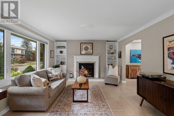 Living room with a sofa, fireplace, built-in shelves, armchair, and large bay windows. - 2189 Blossom Drive, Ottawa