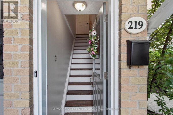 Open front door revealing a staircase with carpeted steps and dark wood trim inside the townhouse. - 219 - 2110 Cleaver Avenue, Burlington
