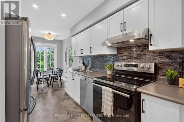Kitchen with white cabinets, stainless steel appliances, dark tiled backsplash, and a small dining area. - 219 - 2110 Cleaver Avenue, Burlington