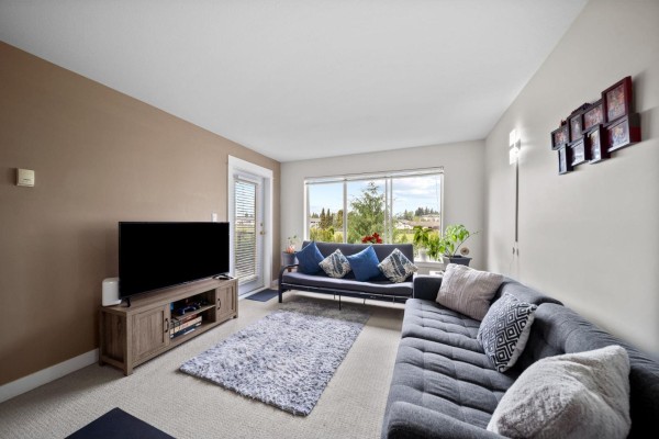 Living room with two grey sofas, a rug, and a large window with a view. - 219 32725 George Ferguson Way, Abbotsford