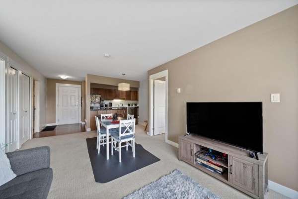 Open-concept living and dining area with a table, sofas, and a large window view. - 219 32725 George Ferguson Way, Abbotsford