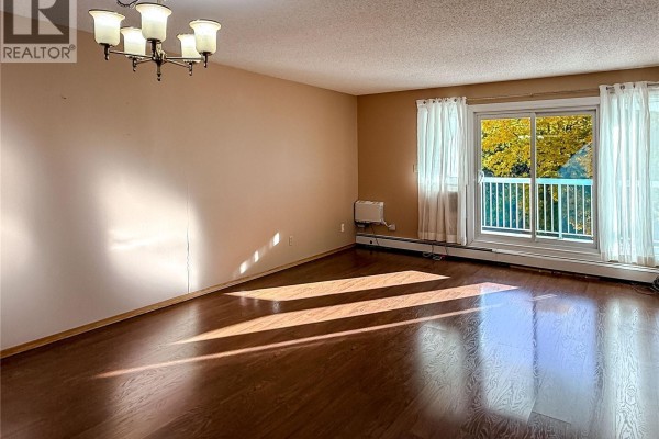 Empty living room with hardwood floors, beige walls, and sliding glass door. - 219 960 Assiniboine Avenue E, Regina