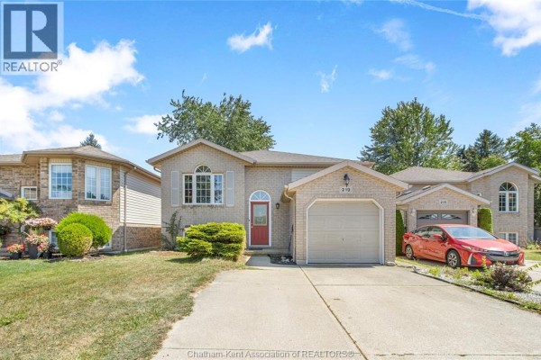 Front exterior of a beige brick house with a red front door and attached garage at sunset. - 219 Greenfield Lane, Chatham