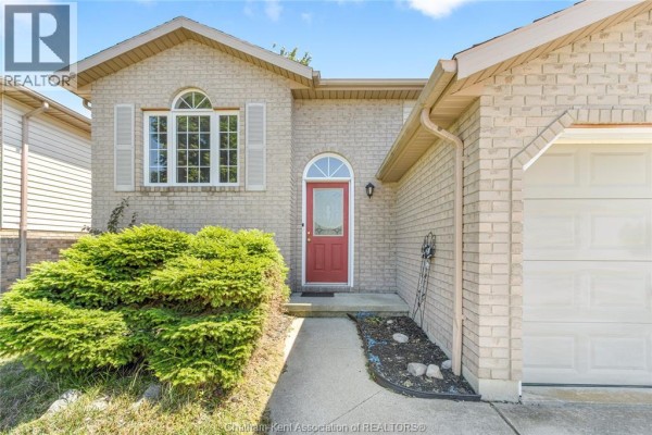 Close-up of the front entrance of a beige brick house with a red door and bushes. - 219 Greenfield Lane, Chatham