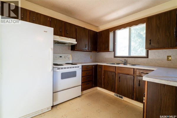Kitchen with white refrigerator, white stove, and dark wood cabinets. - 219 Railway Avenue W, Blaine Lake