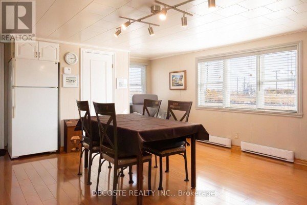 Dining area with a dark brown table set for four, a white refrigerator, and wood flooring. - 21930 Menard Road, North Glengarry