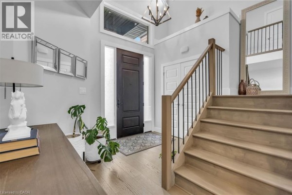 Foyer with a dark wood front door, light wood floors, staircase, and a large mirror. - 2195 Ironwood Road, London