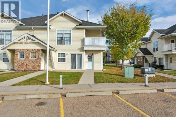 Front exterior of a light yellow townhouse with a concrete walkway and parking. - 22, 33 Jennings Crescent, Red Deer