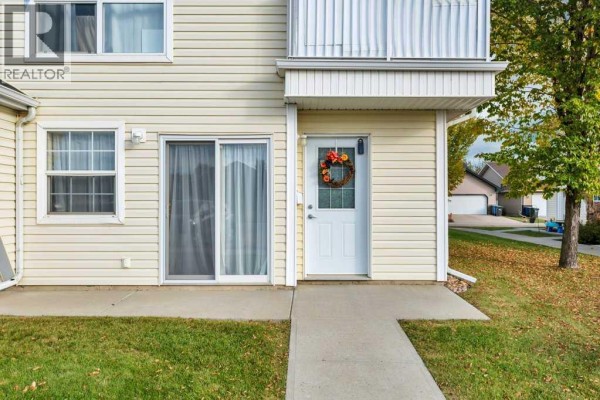 Close-up of townhouse entrance with beige siding, sliding glass door, and white door. - 22, 33 Jennings Crescent, Red Deer