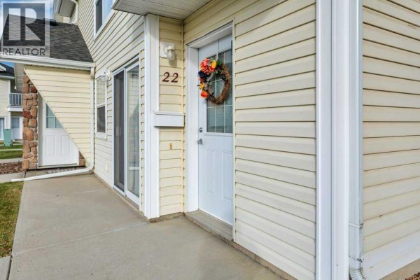 Detail of townhouse entrance showing beige siding, white door with wreath, and address number 22. - 22, 33 Jennings Crescent, Red Deer