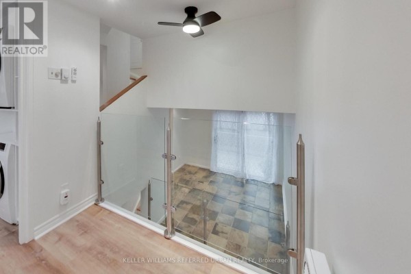 Open-concept living space with stone tile flooring, a staircase, and a glass railing. - 22 - 1666 Queen Street E, Toronto
