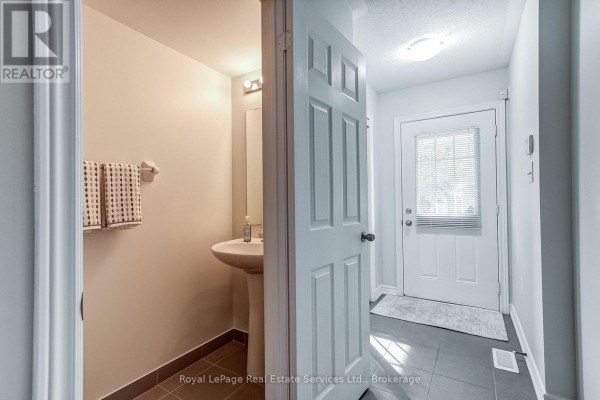 Hallway with light grey walls, dark tile flooring, and a staircase leading to another level. - 22 - 233 Duskywing Way, Oakville