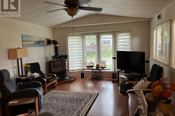 Living room with a wood-burning stove, seating, a television, and a bay window view. - 22 - 4899 Plank Road, Bayham