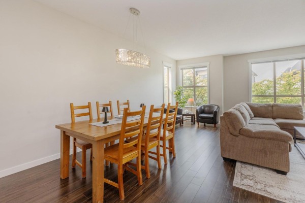 Dining area with a wooden table and chairs, next to a living room with a sectional sofa. - 22 10595 Delsom Crescent, Delta