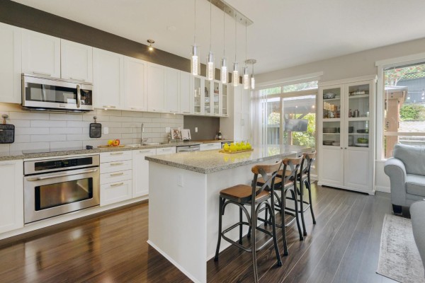 Modern kitchen with white cabinets, granite countertops, stainless steel appliances, and an island with bar stools. - 22 10595 Delsom Crescent, Delta
