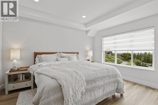 Primary bedroom with a king-size bed, white bedding, and large window with valley view. - 22 10640 248 Street, Maple Ridge